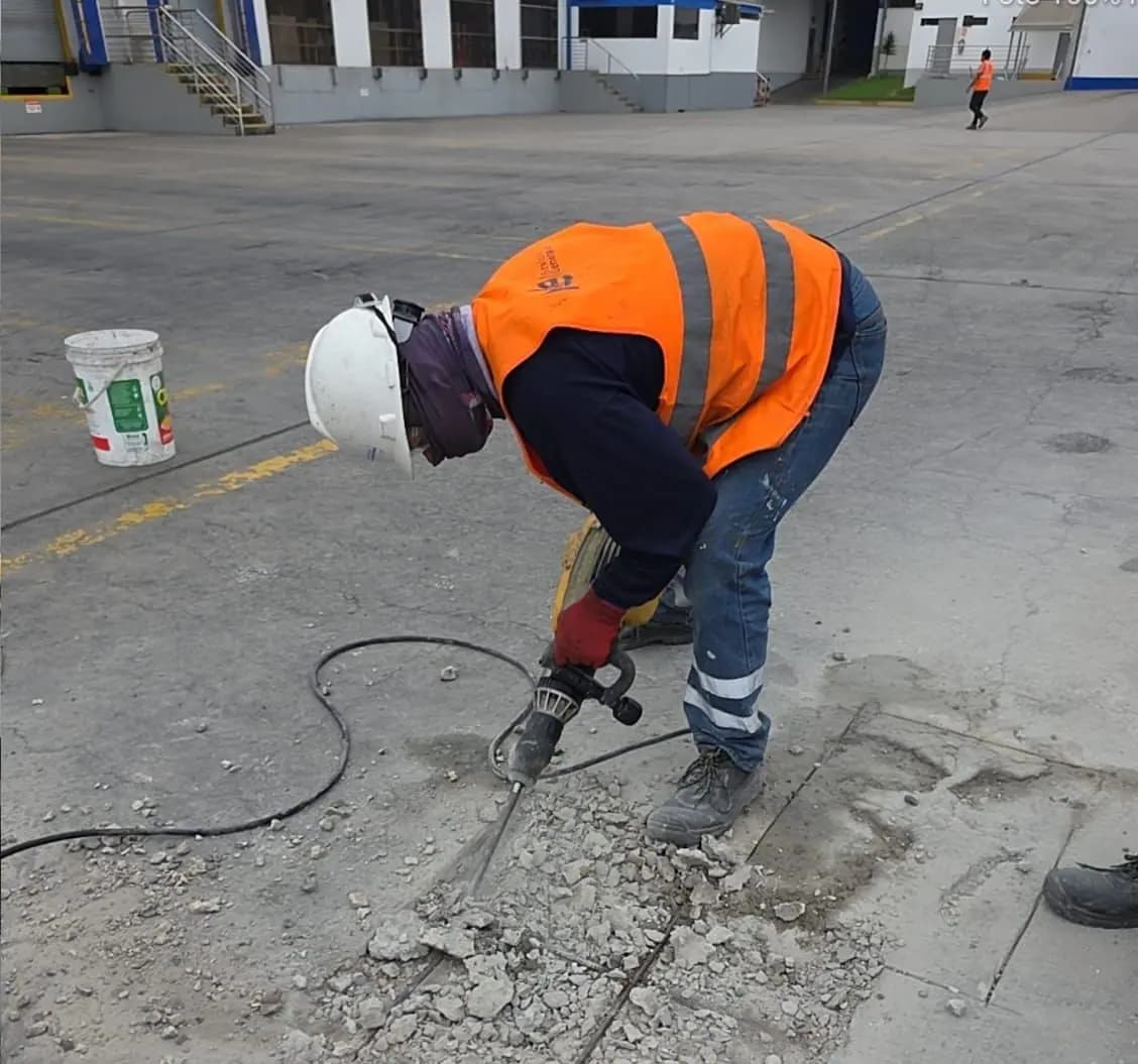 Técnico con equipo de protección picando piso de concreto para su reparación en planta industrial
